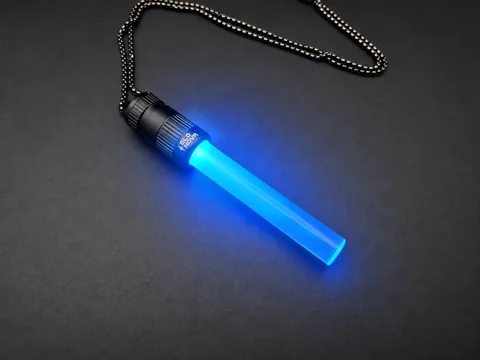 Electric Storm pendant lying on charcoal with its steel ball chain, cyan light filling the clear rod