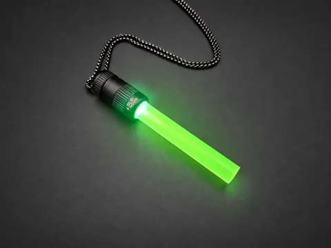 Neon Grove pendant lying on charcoal with its steel ball chain, lime green light filling the clear rod