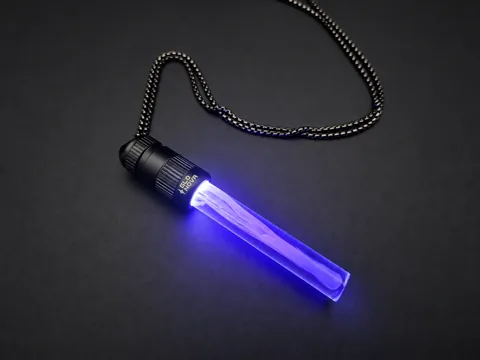 Purple Haze pendant lying on charcoal with its steel ball chain, lavender light flowing through the clear rod