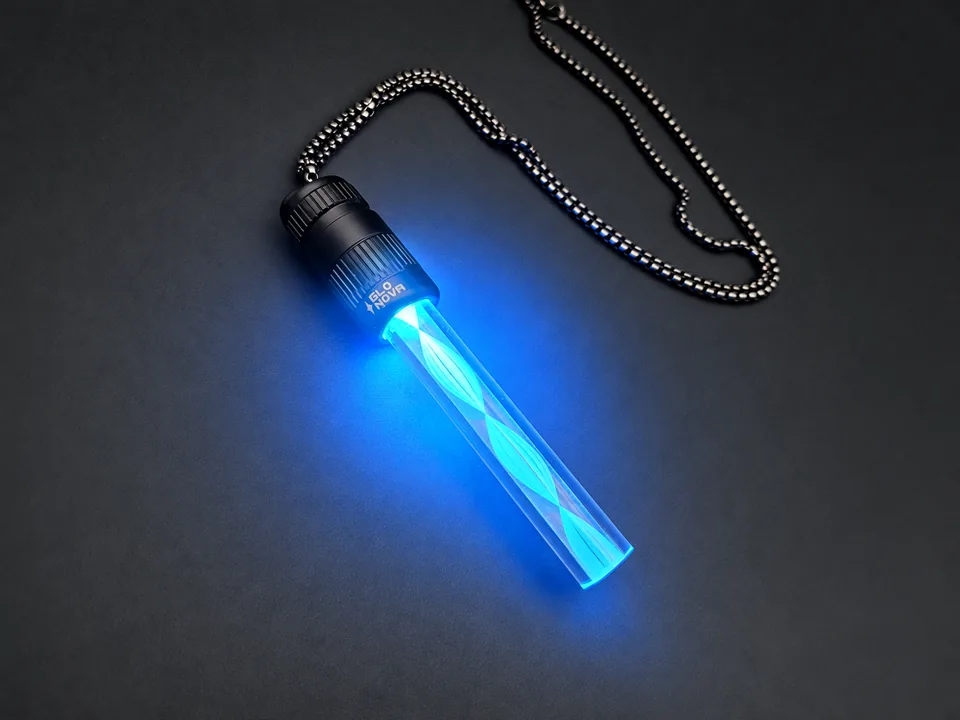 Tidal Drift pendant lying on charcoal with its steel ball chain, a blue spiral of light winding the length of the clear rod